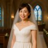 チャペルのバージンロードでオフショルダーのドレスを着た50代の日本人女性がメイクを施し微笑んで立っている様子