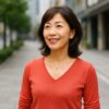 都市の並木道を背景に、自信に満ちた笑顔を見せる50代の日本人女性が活き活きと立っている様子
