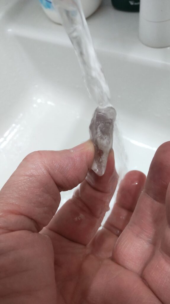 筆者がポイント状のアメジスト原石を指で持ち、水道の流水で表面をすすいでいる様子