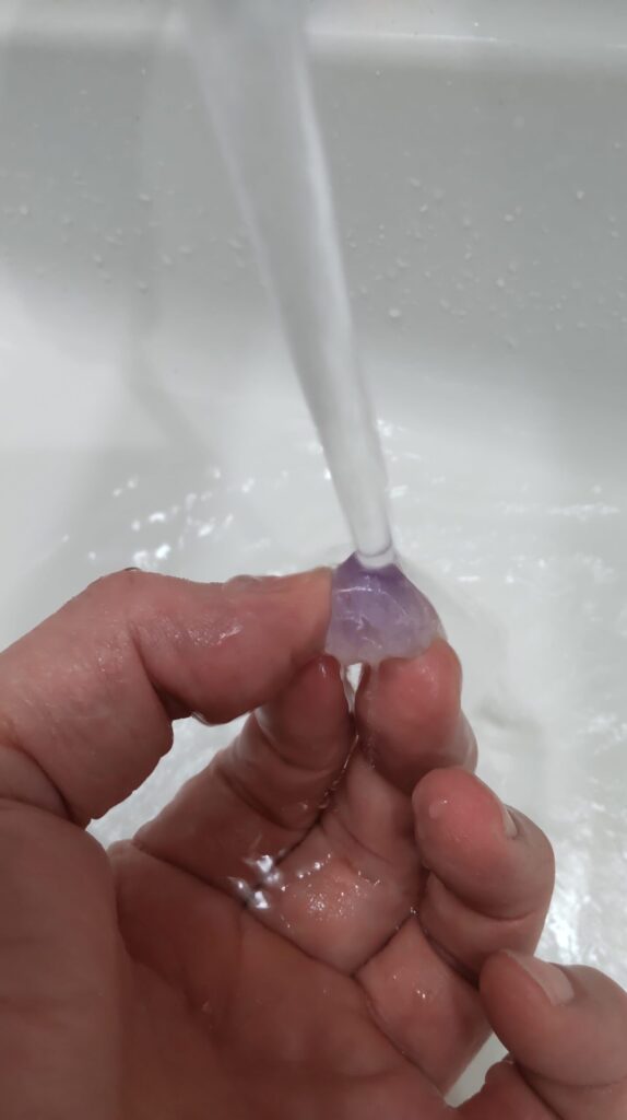 筆者が小さなアメジスト原石を指で持ち、水道の流水ですすいでいる様子