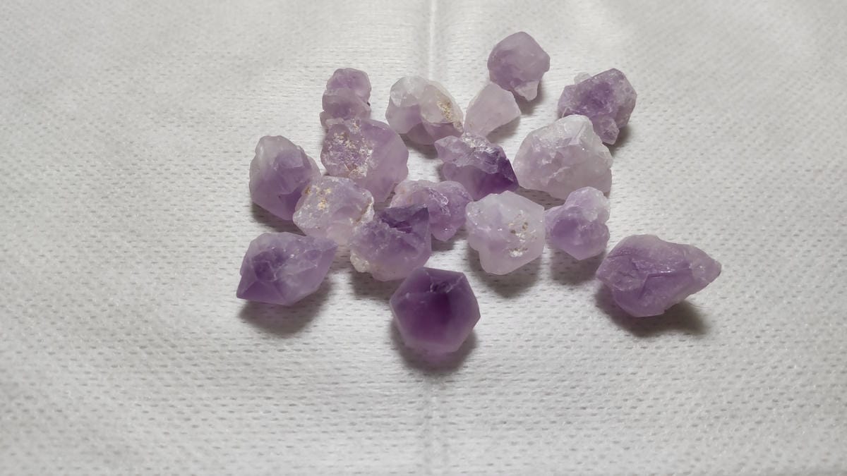 アメジストとは?紫水晶の特徴・硬度・成分を鉱物学から解説 白い背景に広げた、紫色の濃淡や白っぽい部分、形が異なるアメジストの原石