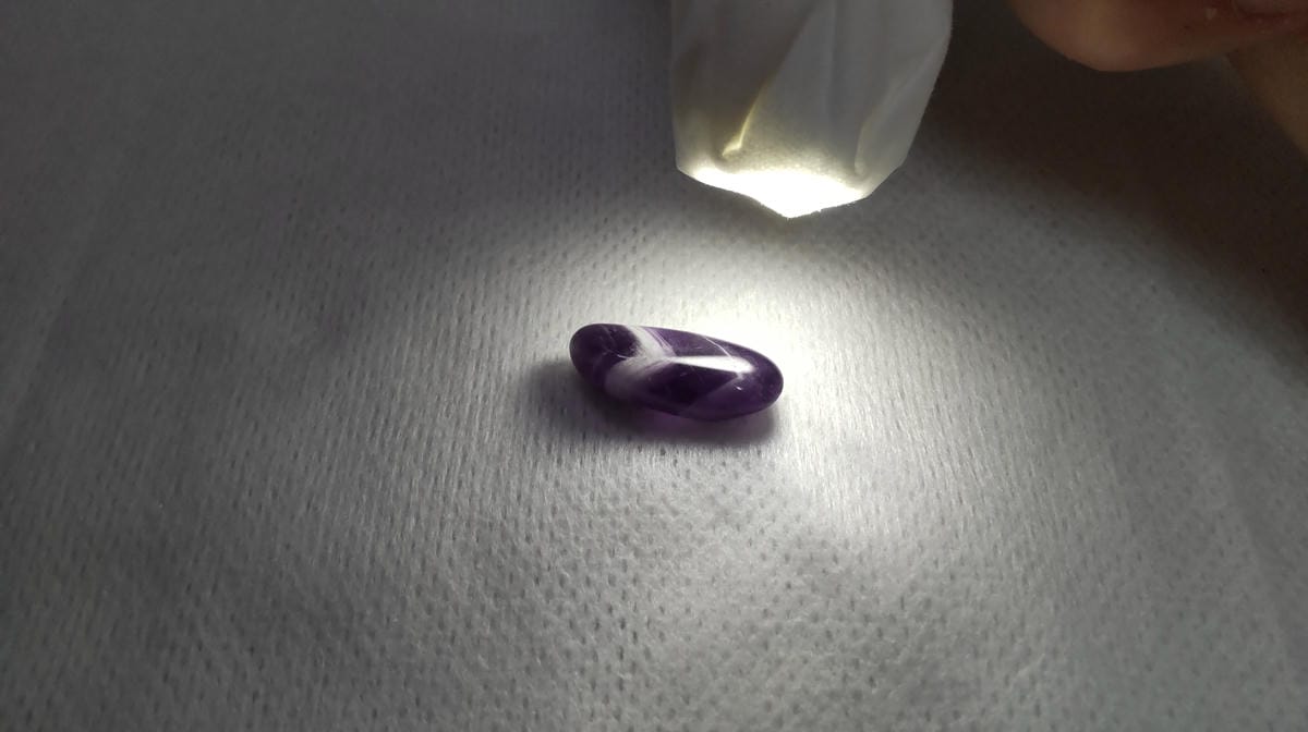 白いV字状の帯がある紫色の粒に、上方からライトを当てた様子