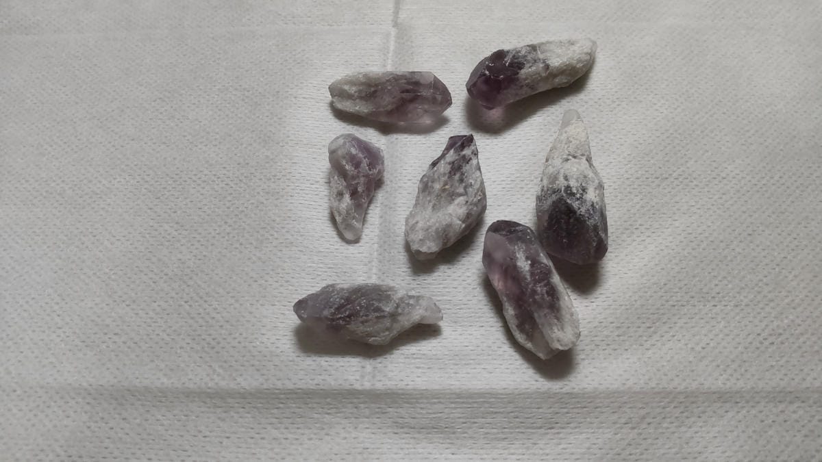 アメジストとは?紫水晶の特徴・硬度・成分を鉱物学から解説 紫色と白っぽい部分があるポイント状のアメジスト原石7個を、間隔を空けて並べた様子