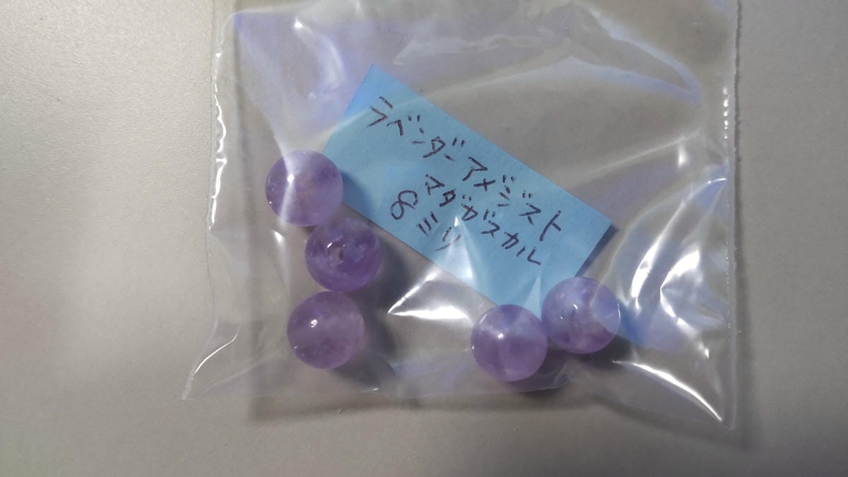 アメジストとは?紫水晶の特徴・硬度・成分を鉱物学から解説 ラベンダーアメジスト、マダガスカル、8ミリと書かれたタグと、袋に入った淡い紫色の丸玉ビーズ5粒